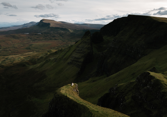 An eloping couple stand on the edge of a cliff at the Quiraing isle of Skye, a photo taken by Oli and Steph Photography
